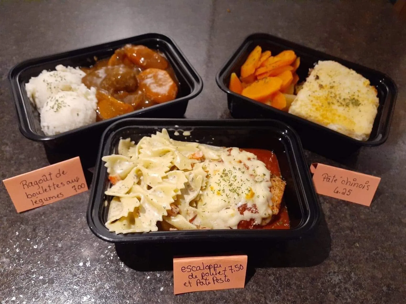 Portions de ragoût de boulettes, escalope de poulet aux pâtes et pâté chinois en contenants, avec étiquettes de prix manuscrites.